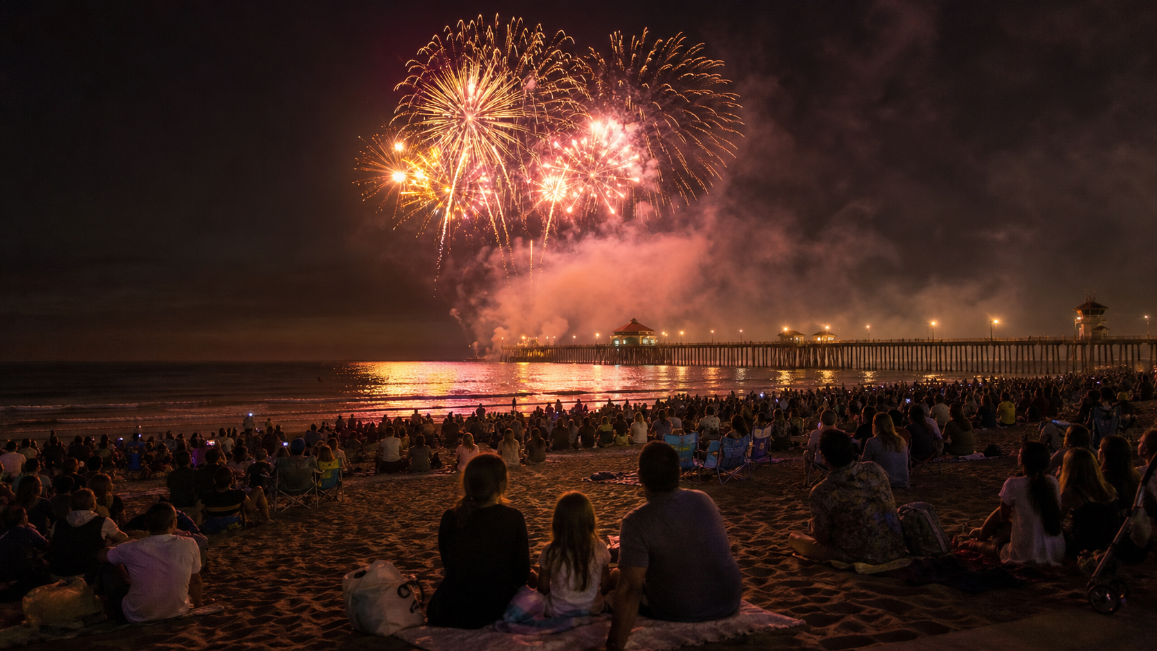 Fireworks over the ocean near a pier with families watching from the beach